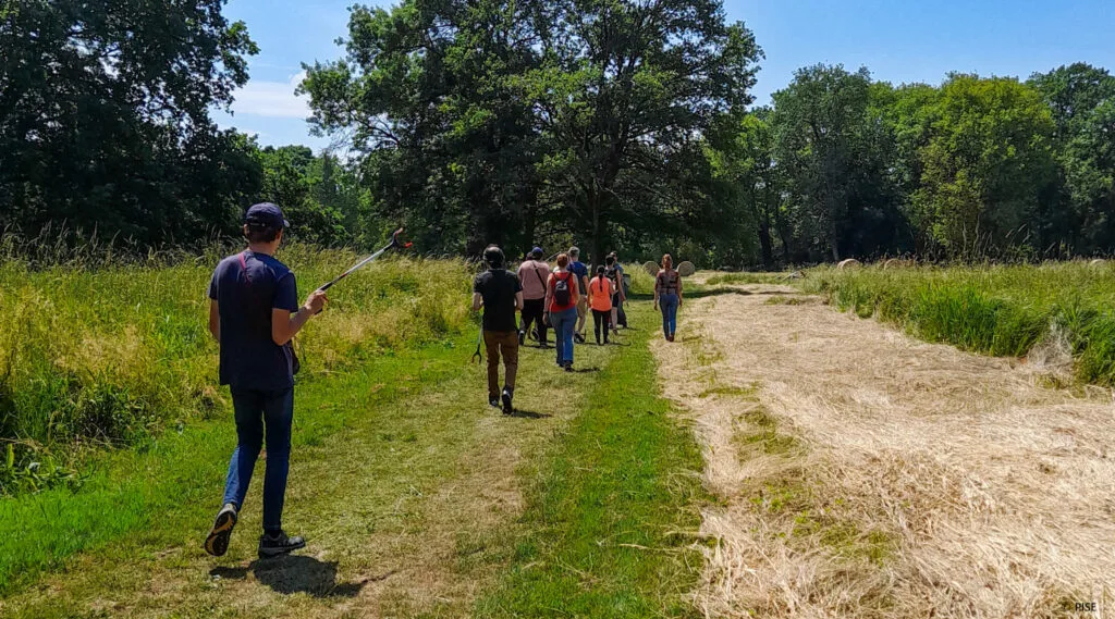 Photo des participants à la promenade et collecte de déchets sauvages, où l'on peut voir une dizaine de personnes, marcher dans une forêt, équipés de pinces pour ramasser les déchets.