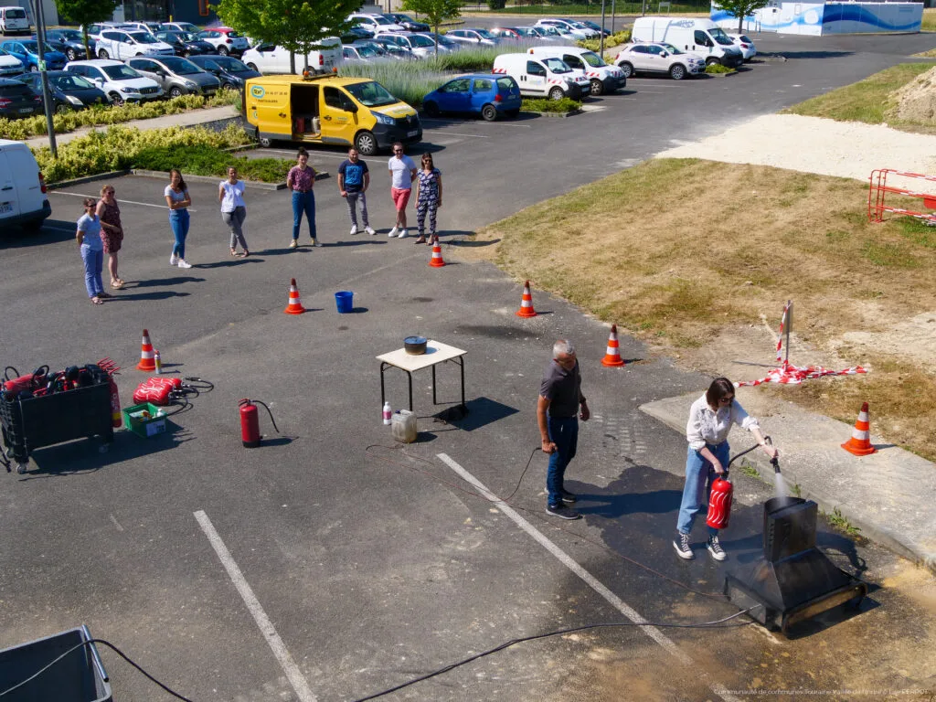 Photo de 9 agents entrain de suivre une formation à l'utilisation des extincteurs. Une agente est entrain de s'entrainer à l'utilisation d'extincteur, sous la vigilance du pompier, qui encadre cette formation.