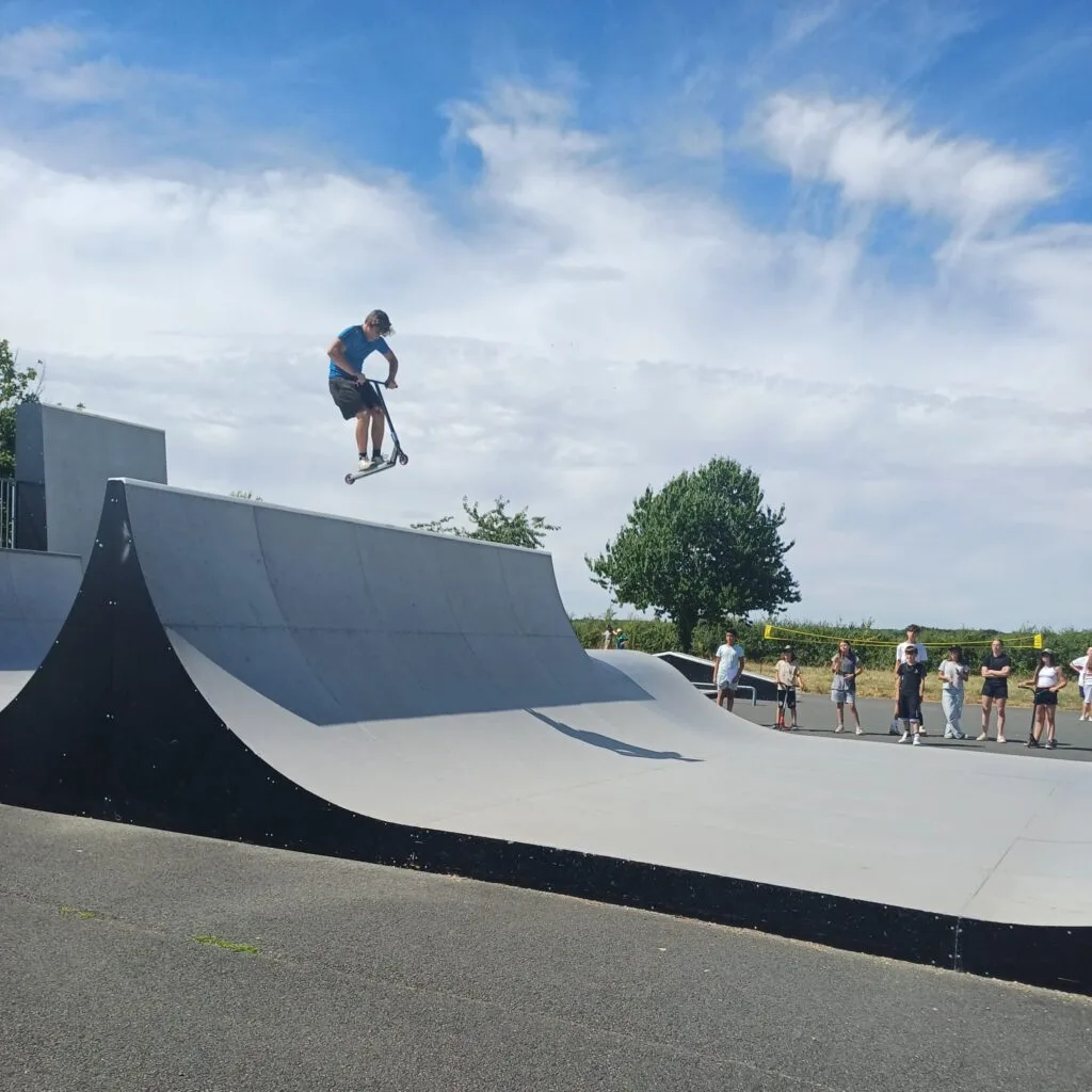 Un jeune en trottinette plane au dessus d'un module de skate