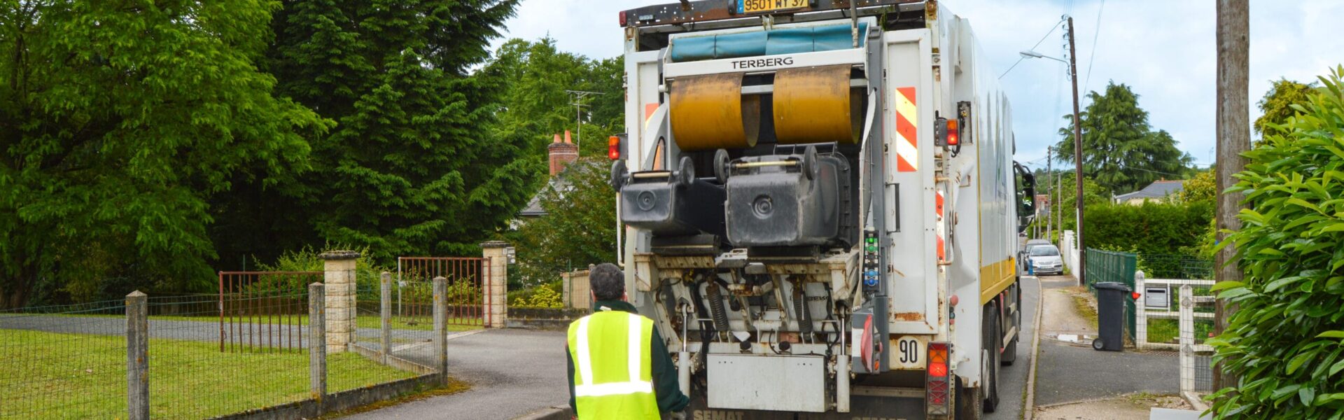 Photo d'un ripeur en tenue de sécurité jaune se tenant debout un camion de collecte pendant sa tournée de ramassage des déchets.