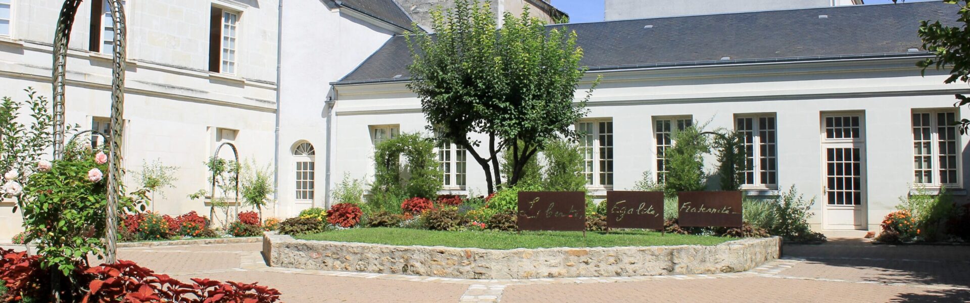 Photo de la cour intérieure de la Mairie d'Azay-le-Rideau, la cour est végétalisée et fleurie. On peut y voir des panonceaux "Liberté, Égalité, Fraternité".